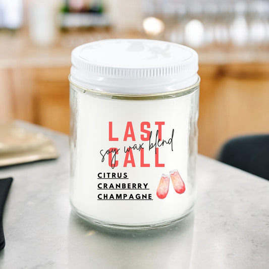 A white jar candle with a label that reads 'Last Call' followed by 'Citrus Cranberry Champagne', placed on a kitchen countertop.